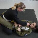 Das Foto zeigt zwei Frauen im Gi in der so genannten Closed Guard, bei der eine Frau die Hüften der anderen mit den eigenen Beinen umschlungen hat, während sie selbst auf dem Boden liegt.