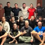 Das Foto zeigt einen Großteil der Teilnehmer*innen der Benefiz Open Mat, die in drei Reihen sitzend, kniend und stehend posieren.